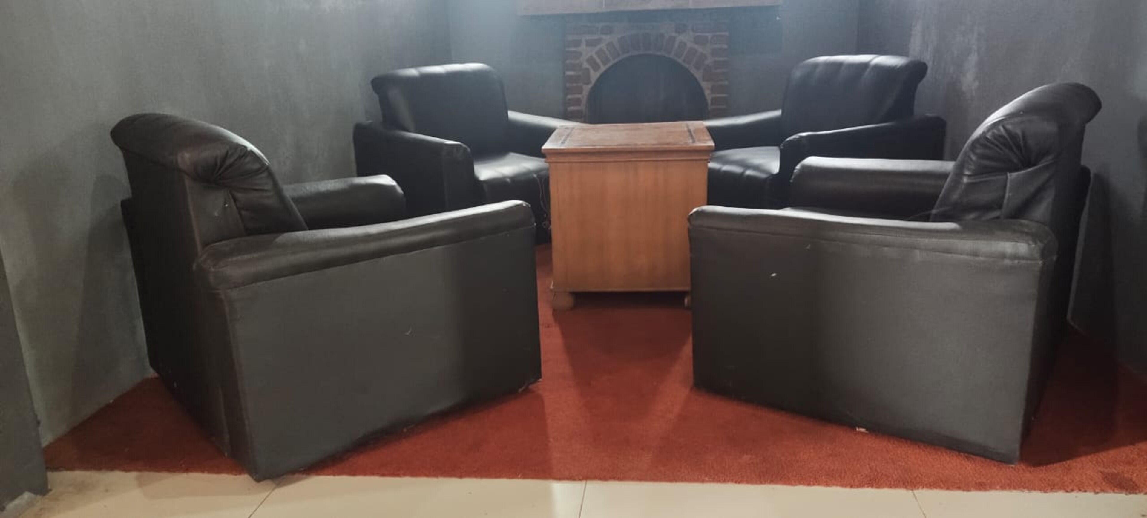 A room with four black leather sofas arranged around a wooden coffee table.