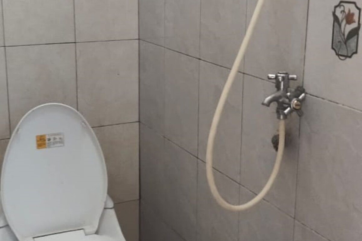 A bathroom with a toilet, a shower, and a bucket.