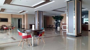 Een ruime lobby met een ronde centrale tafel en stoelen, een receptiebalie en een grote plant.