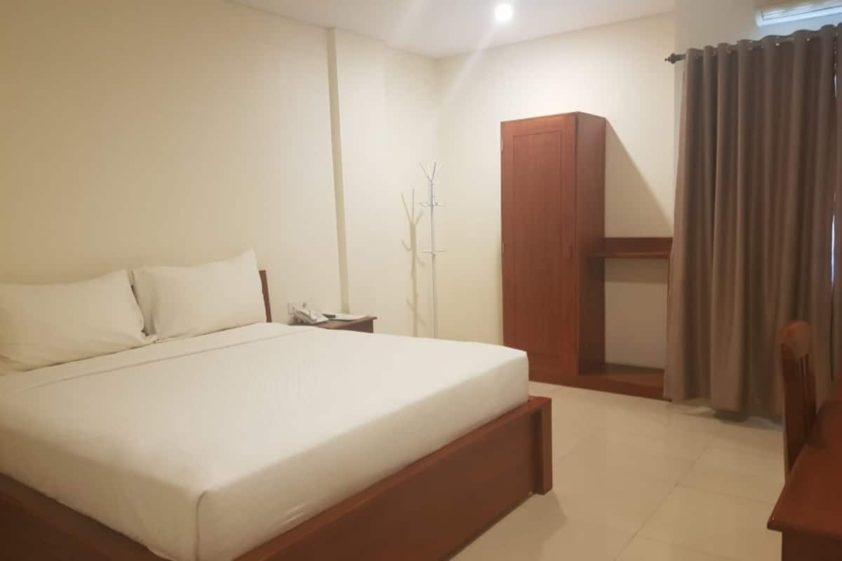 A bedroom with a large bed, a wooden wardrobe, a bedside table with a lamp, and a window with curtains.
