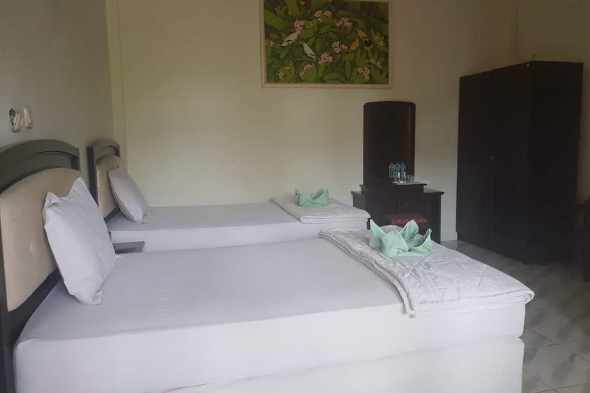 A hotel room with two beds, a painting on the wall, a wardrobe, and a small table with toiletries.
