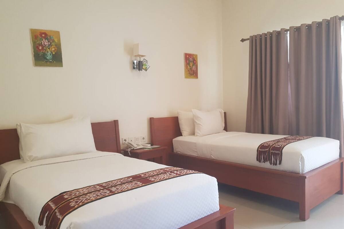 A hotel room with two beds, a bedside table with a phone, a wall-mounted light, and a curtain.