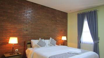 Un dormitorio con pared de ladrillo, una cama con ropa de cama blanca, dos lámparas de noche y una ventana con cortinas.