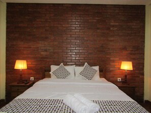 A hotel room with a brick wall, a bed with white bedding, two bedside lamps, and patterned pillows. - Nia Maretta House Syariah (Borobudur)