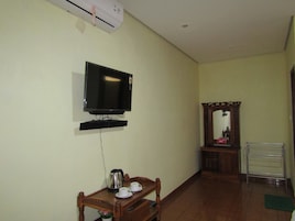 Una habitación con una televisión montada en la pared, una mesa de madera con un hervidor y tazas, un espejo y un radiador.