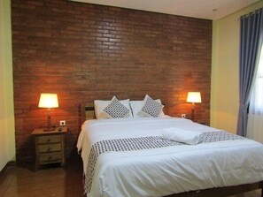 Een hotelkamer met een bakstenen muur, een bed met wit beddengoed, twee bedlampen en een nachtkastje van hout.