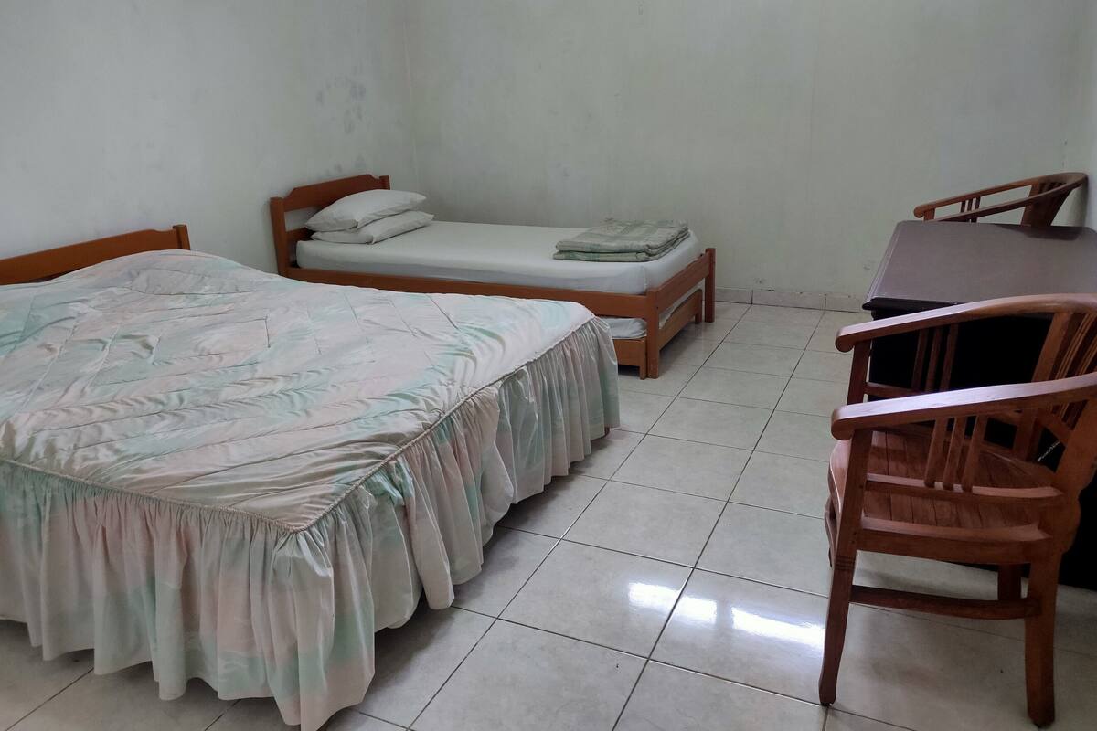 A small, clean room with two single beds, a wooden desk, and a chair.