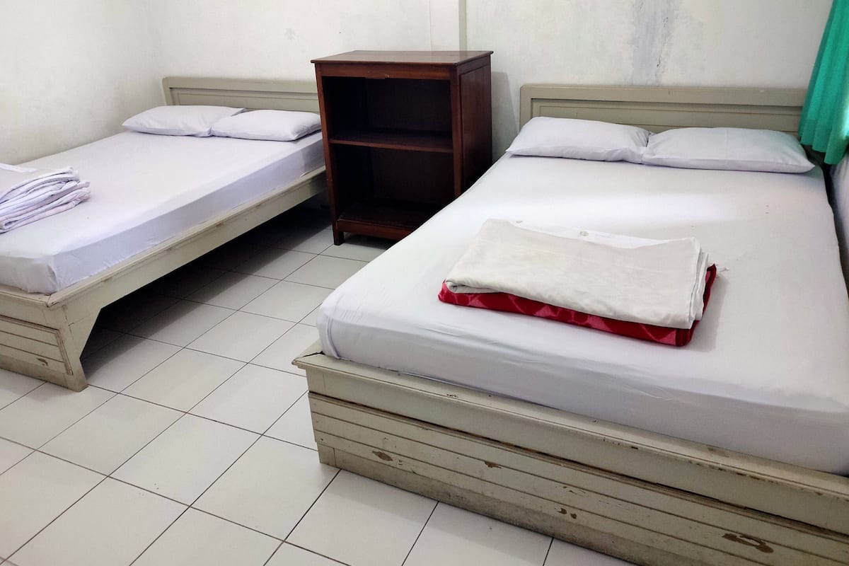 Two single beds with wooden headboards and white bedding, a small wooden nightstand, and a green curtain.