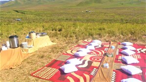 An outdoor picnic setup with a blanket, pillows, and a table with food and drink containers. - Rahayu Jawarika Bromo Hotel (Ngadisari)