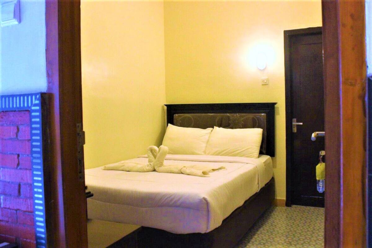 A hotel room with a bed, a door, and a wall-mounted light.