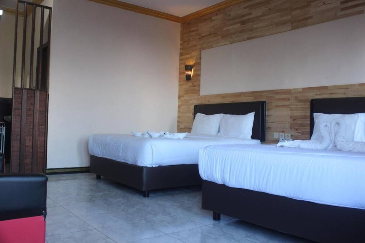 A hotel room with two beds, a wooden accent wall, and a tiled floor.