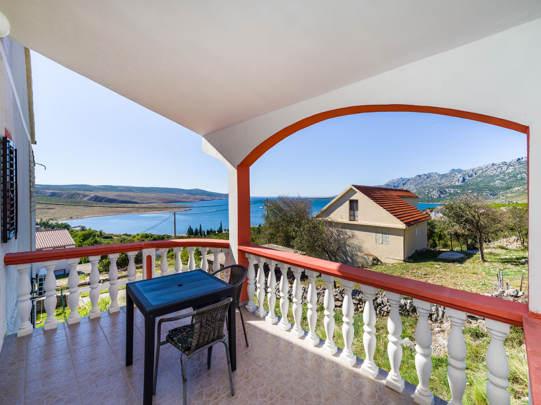 Varanda com mesa e cadeira, oferecendo uma vista panorâmica de um lago e montanhas.