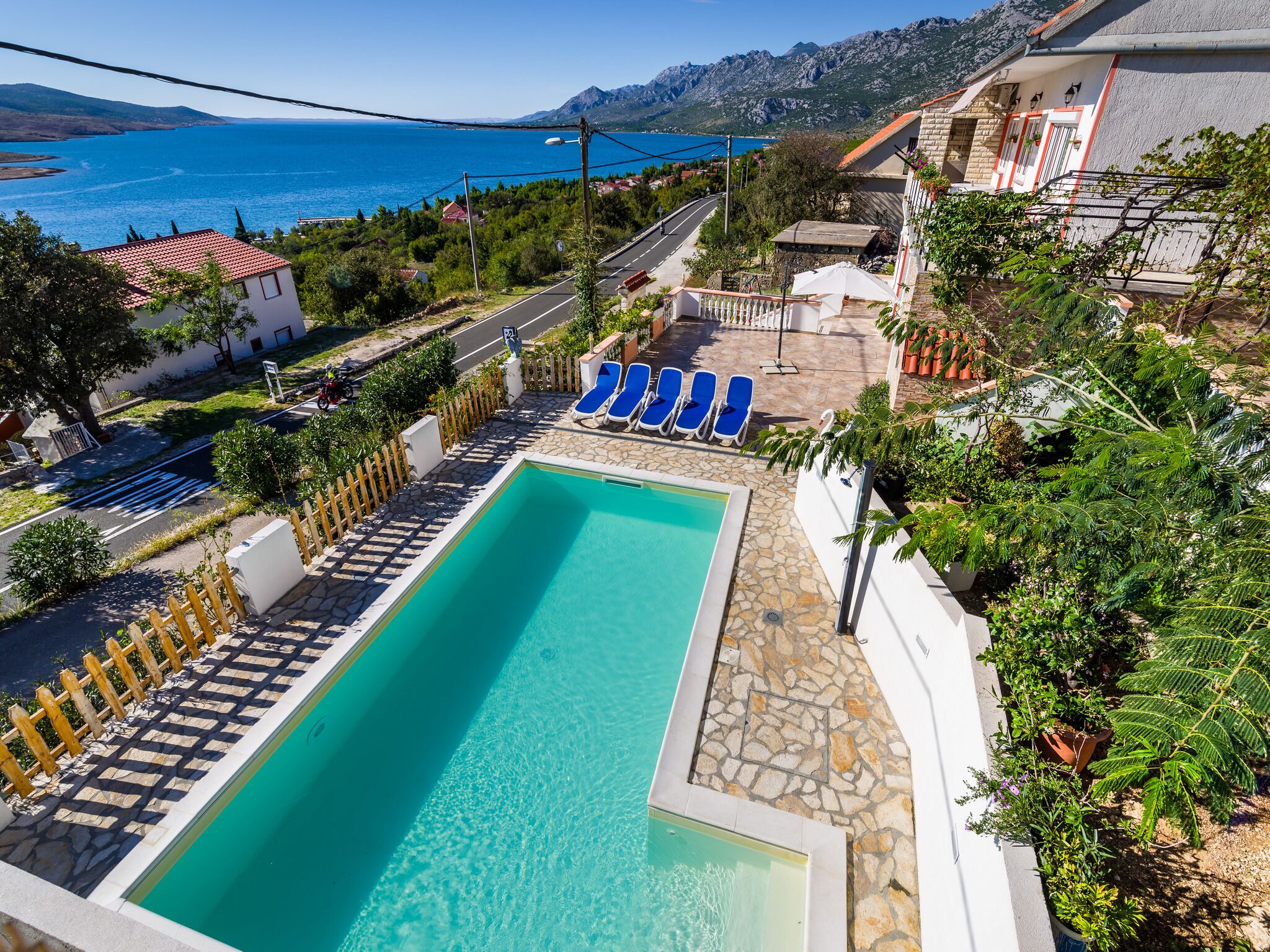 A rectangular swimming pool with a stone deck, surrounded by a wooden fence and blue lounge chairs.