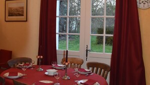 A dining room with a table set for four, a clock on the wall, and a window with curtains.