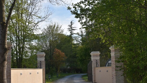 A gravel driveway leading to a gated entrance with brick walls and a metal gate.