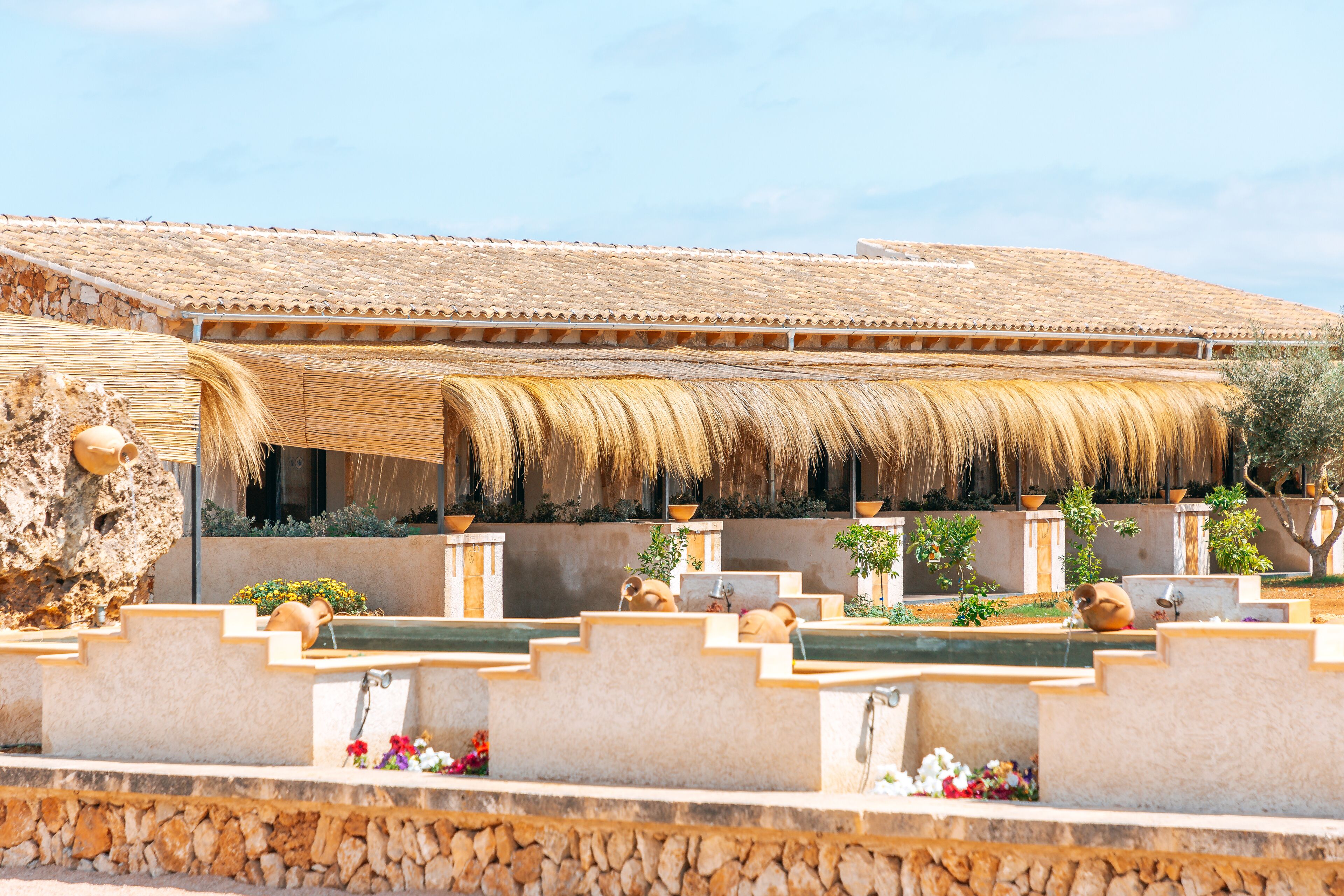 Il s’agit d’un bâtiment traditionnel doté d’un toit en tuiles et d’une charpente en chaume. Des marches mènent à un élément décoratif aquatique agrémenté de fleurs.