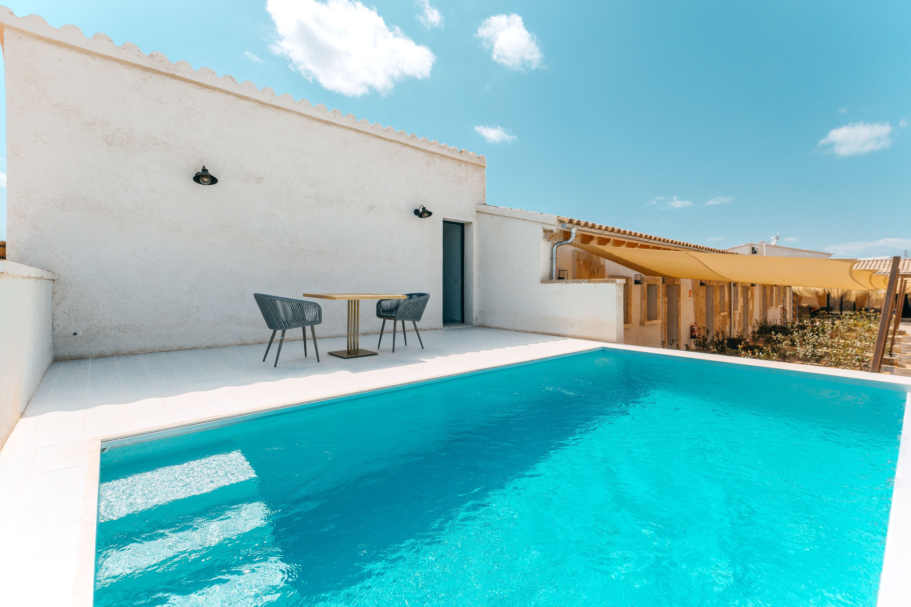 Una piscina con una parete bianca e una porta, due sedie e un tavolo.