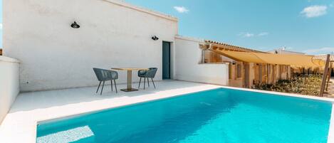 Una piscina con una parete bianca e una porta, due sedie e un tavolo.