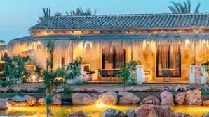 Il s’agit d’un bâtiment traditionnel, doté d’un toit en tuiles, d’un patio couvert avec des sièges et d’un petit étang agrémenté de rochers.