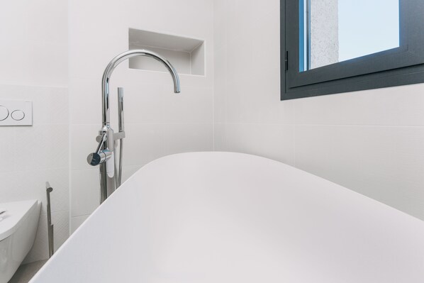 Un baño moderno con una bañera independiente, un cabezal de ducha empotrado y una ventana que deja entrar luz natural.