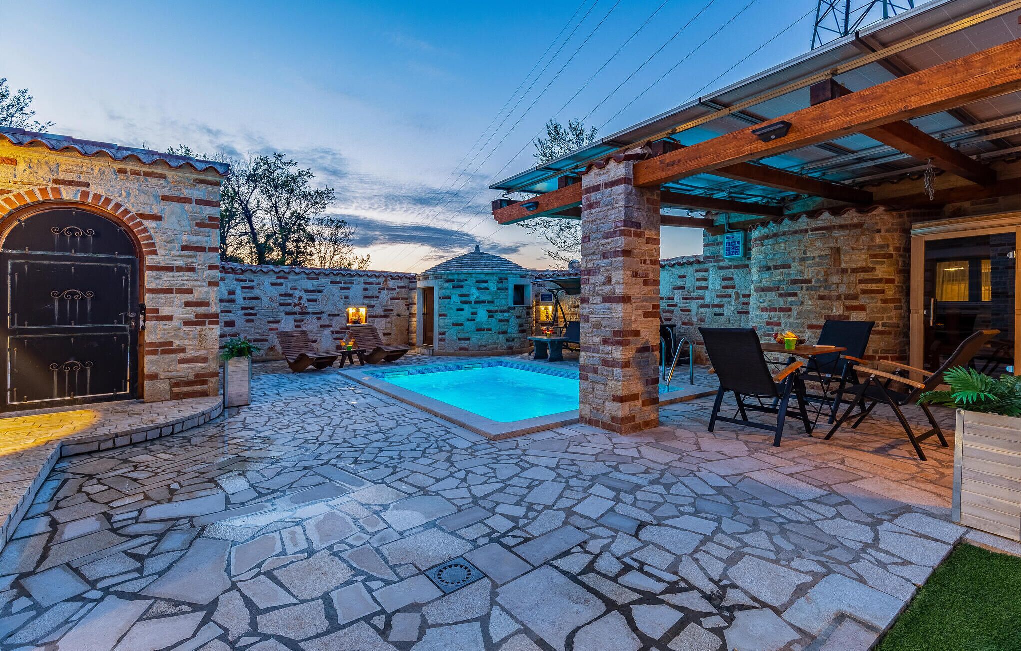 Une terrasse en pierre avec une piscine, un espace salon extérieur et un mur en briques.