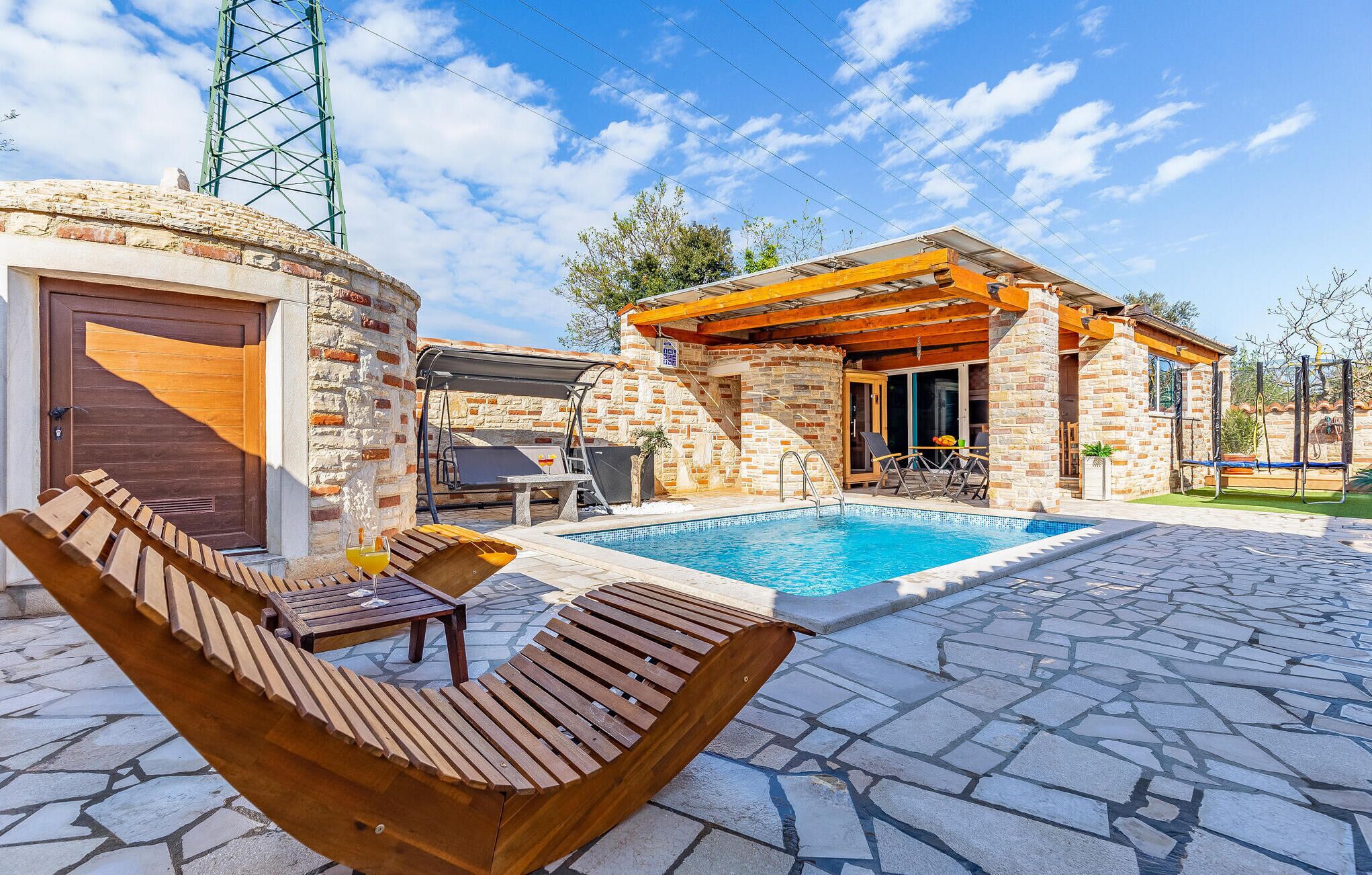 Un espace aménagé au bord de la piscine, avec une terrasse en pierre, des chaises longues en bois et un petit coin salon extérieur comprenant une table et des chaises.