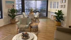 Un salón amplio con un ventanal grande, un comedor con mesa y sillas redondas, y varias plantas en macetas.