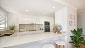 Una cocina moderna con armarios blancos, una isla central y taburetes de bar.