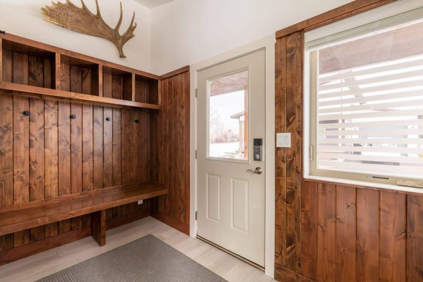 A wooden entryway with a bench, a door with a keypad lock, and a large window with blinds.
