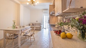 Uma cozinha moderna com área de refeições, apresentando bancada branca, um candelabro e vista para a sala de estar.
