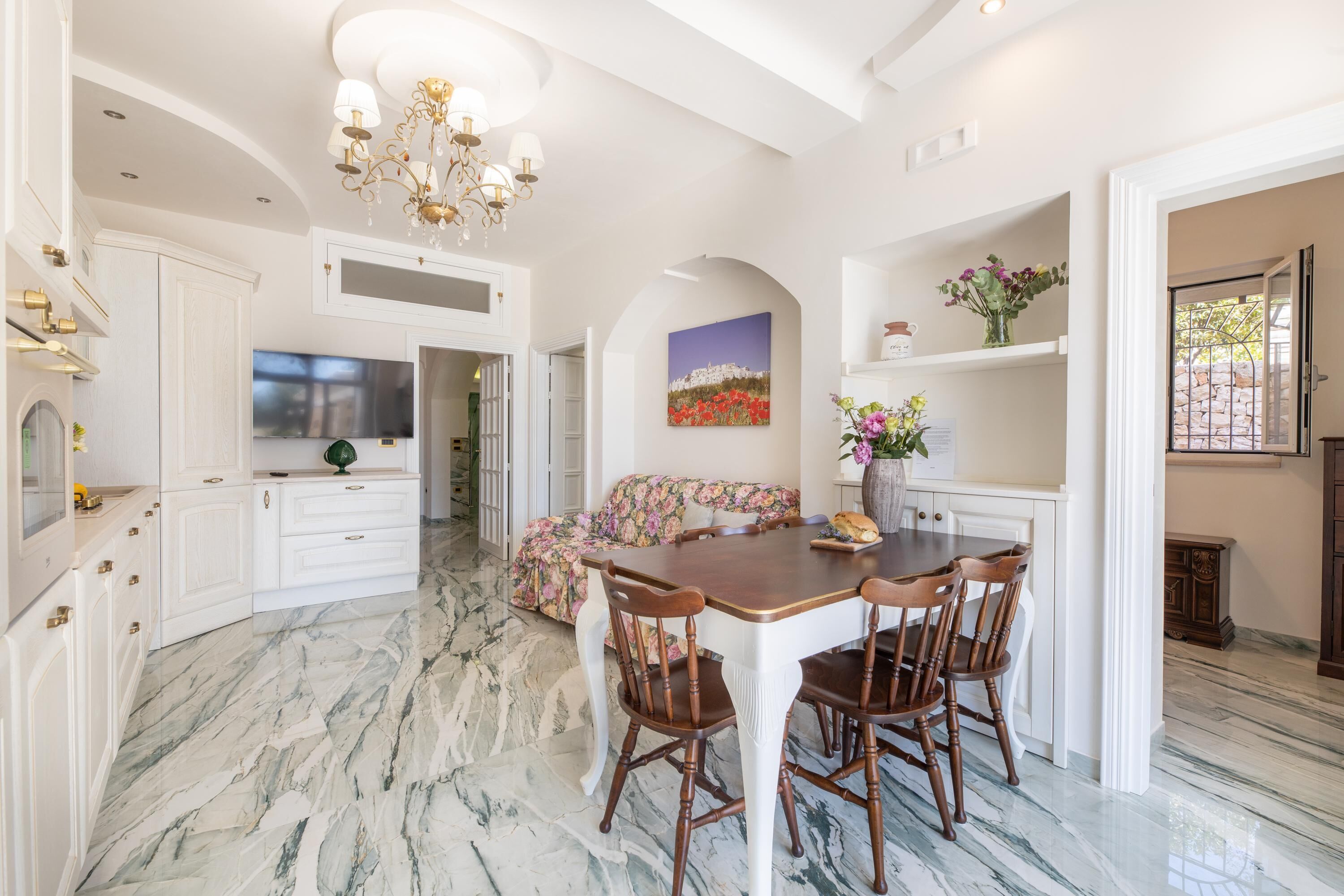 Una cocina amplia con armarios blancos, piso de mármol y un comedor con sillas de madera.