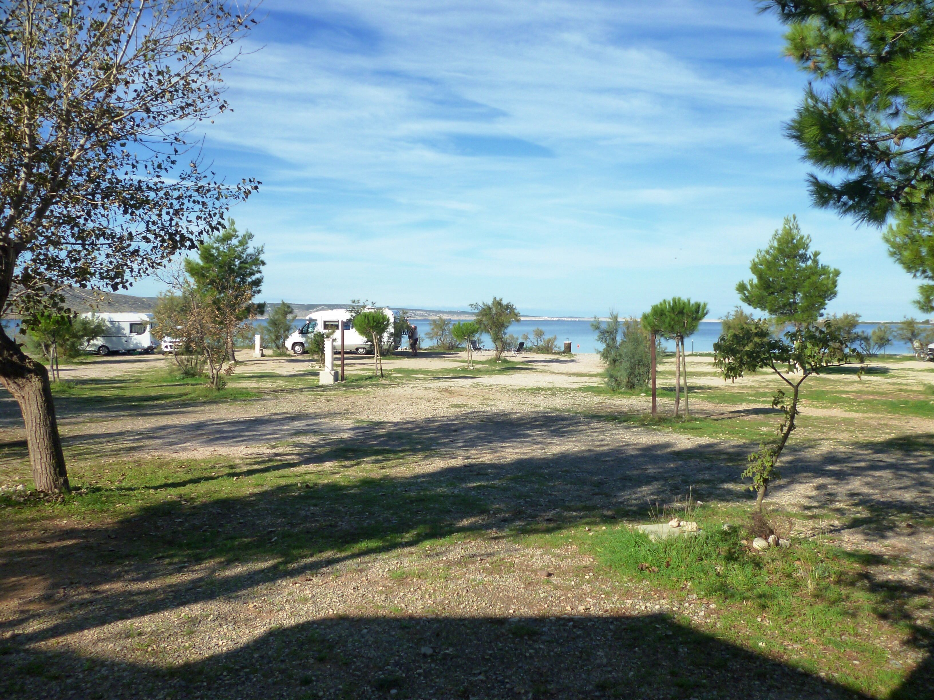 A campsite with a gravel path, trees, and a body of water in the background.