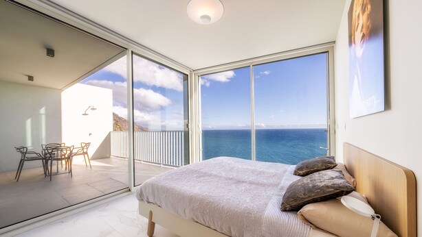 Une chambre avec un grand lit, une vue sur la mer et un balcon équipé d’une table et de chaises.