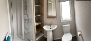 A bathroom with a glass-enclosed shower, a white sink, a toilet, and a mirror above the sink. - Charming 3-bed Holiday Home at Primrose Valley (Filey)