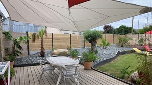 A wooden deck with a table and chairs, surrounded by potted plants and a small garden area. - Villa 6 pl 400 m from the sea (Cléder)