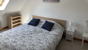 A bedroom with a sloped ceiling, a bed with floral bedding, two patterned pillows, a nightstand with a lamp, and a wall-mounted painting. - Villa 6 pl 400 m from the sea (Cléder)
