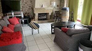 A living room with a stone wall, a fireplace, a television, and a bar area. - Villa 6 pl 400 m from the sea (Cléder)