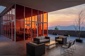 Un espace extérieur moderne aménagé avec des sièges, une structure en verre, une table à manger et des chaises.