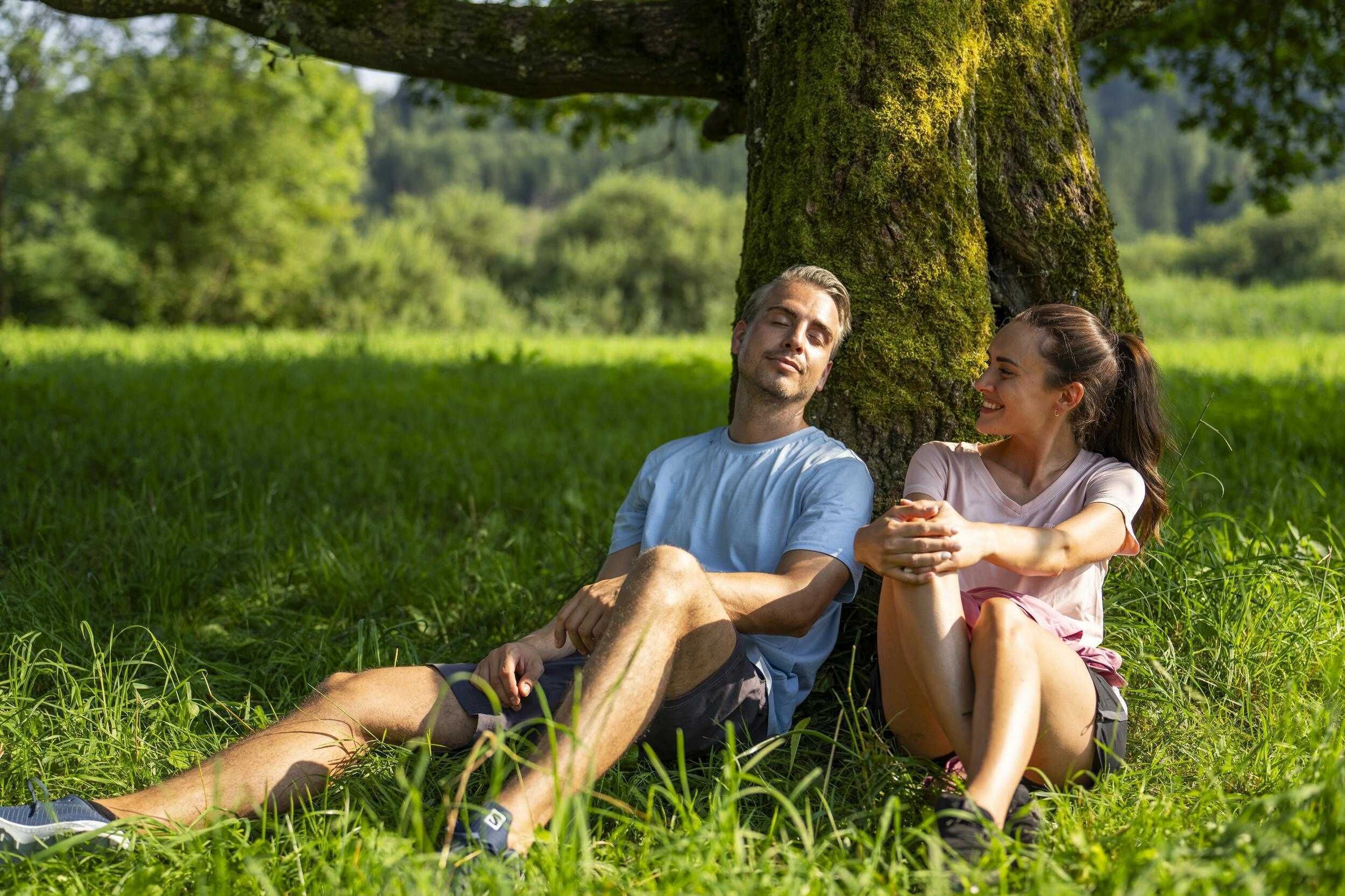 Two people sitting on grass under a tree in a park.