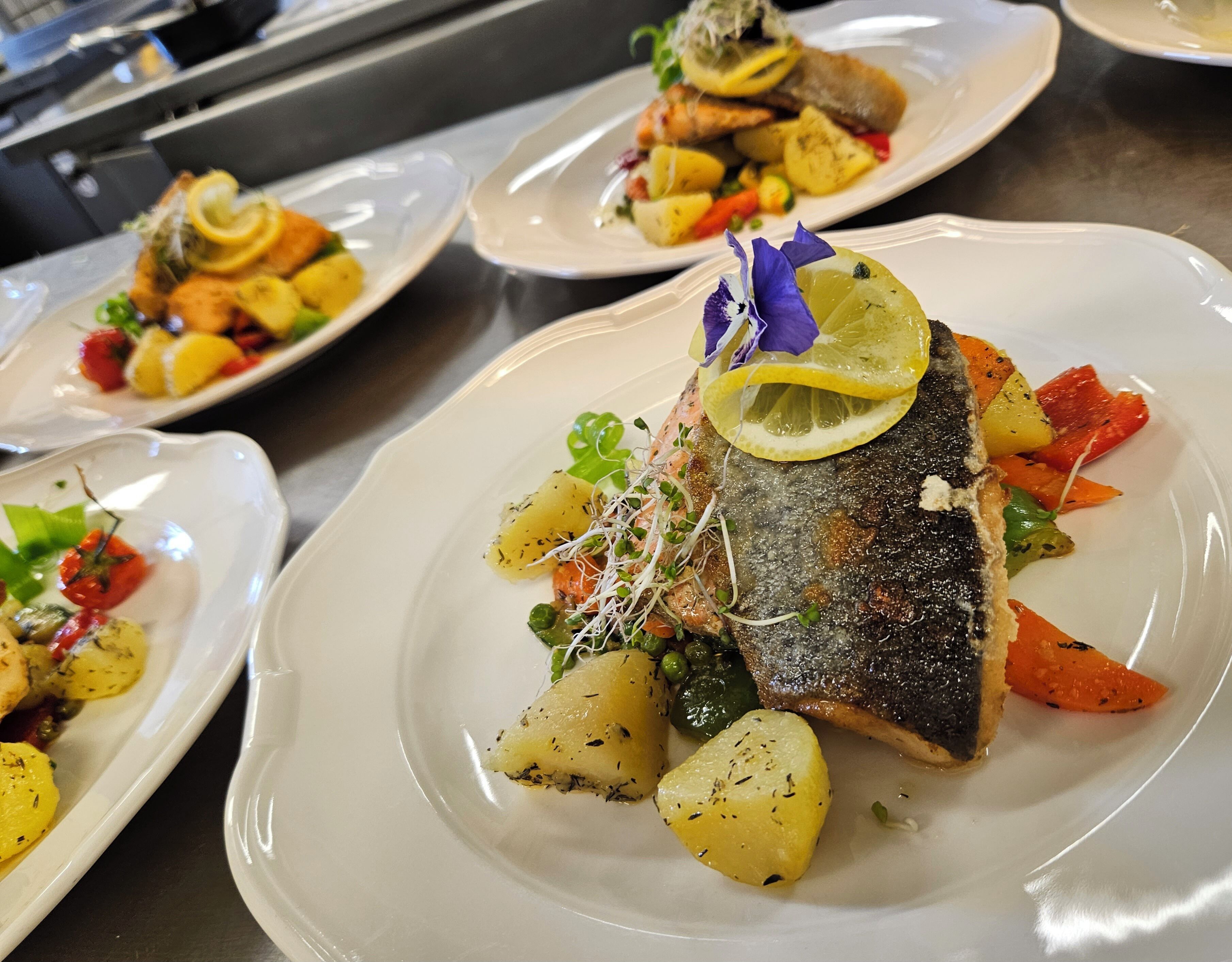 A restaurant setting with multiple plates of food, including fish and vegetables.