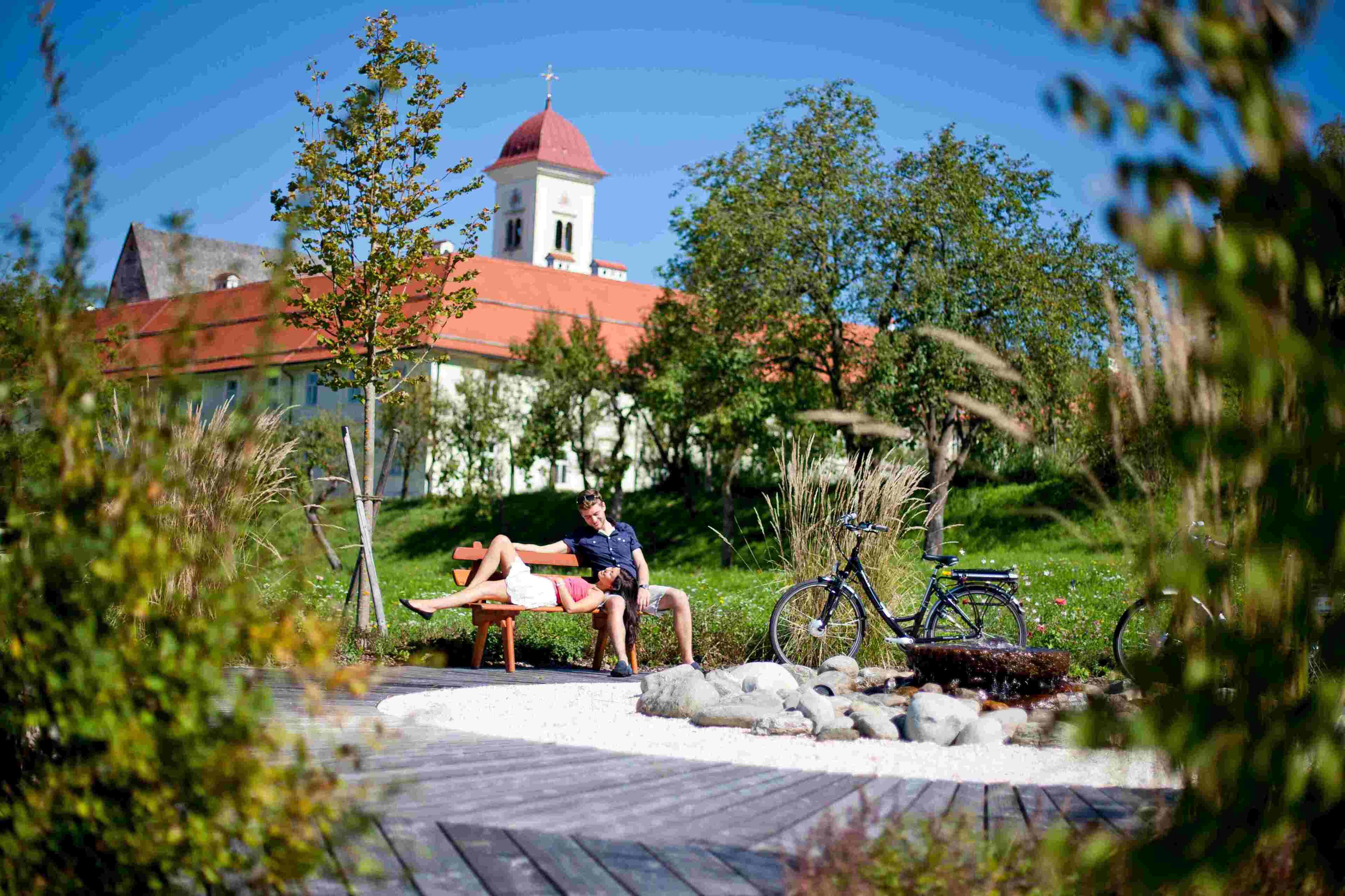 A wooden deck with a bench, a bicycle, and a stone fountain.