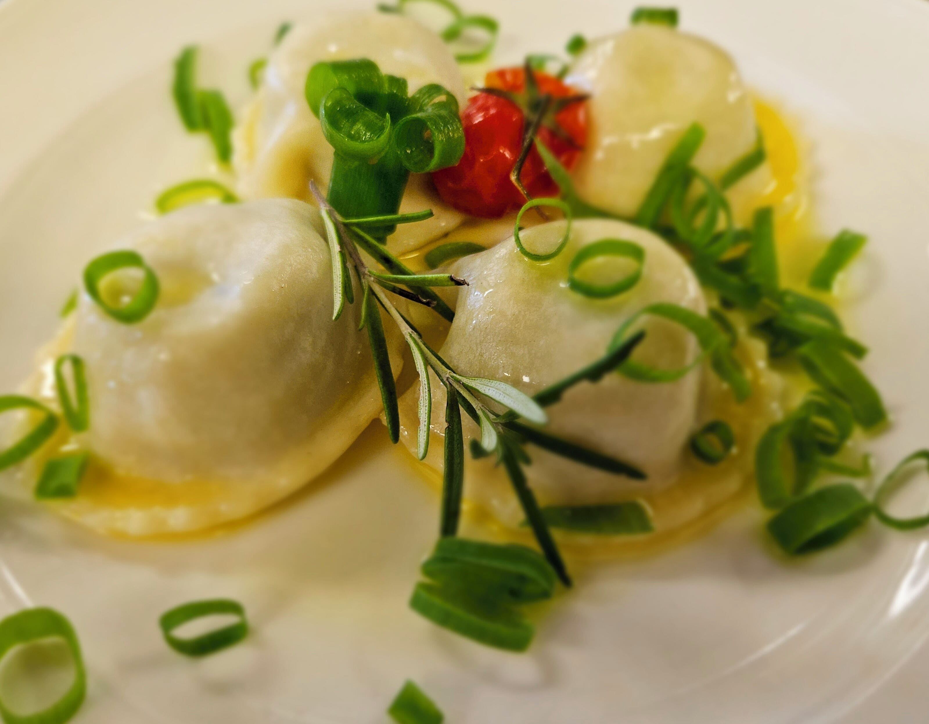 Une assiette de raviolis garnis d’oignons verts et d’une branche de romarin.