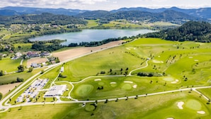 Vue aérienne d’un terrain de golf avec un lac, entouré de montagnes et de zones résidentielles.