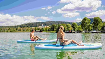Two individuals sitting on paddleboards on a calm lake with a forested hill in the background.