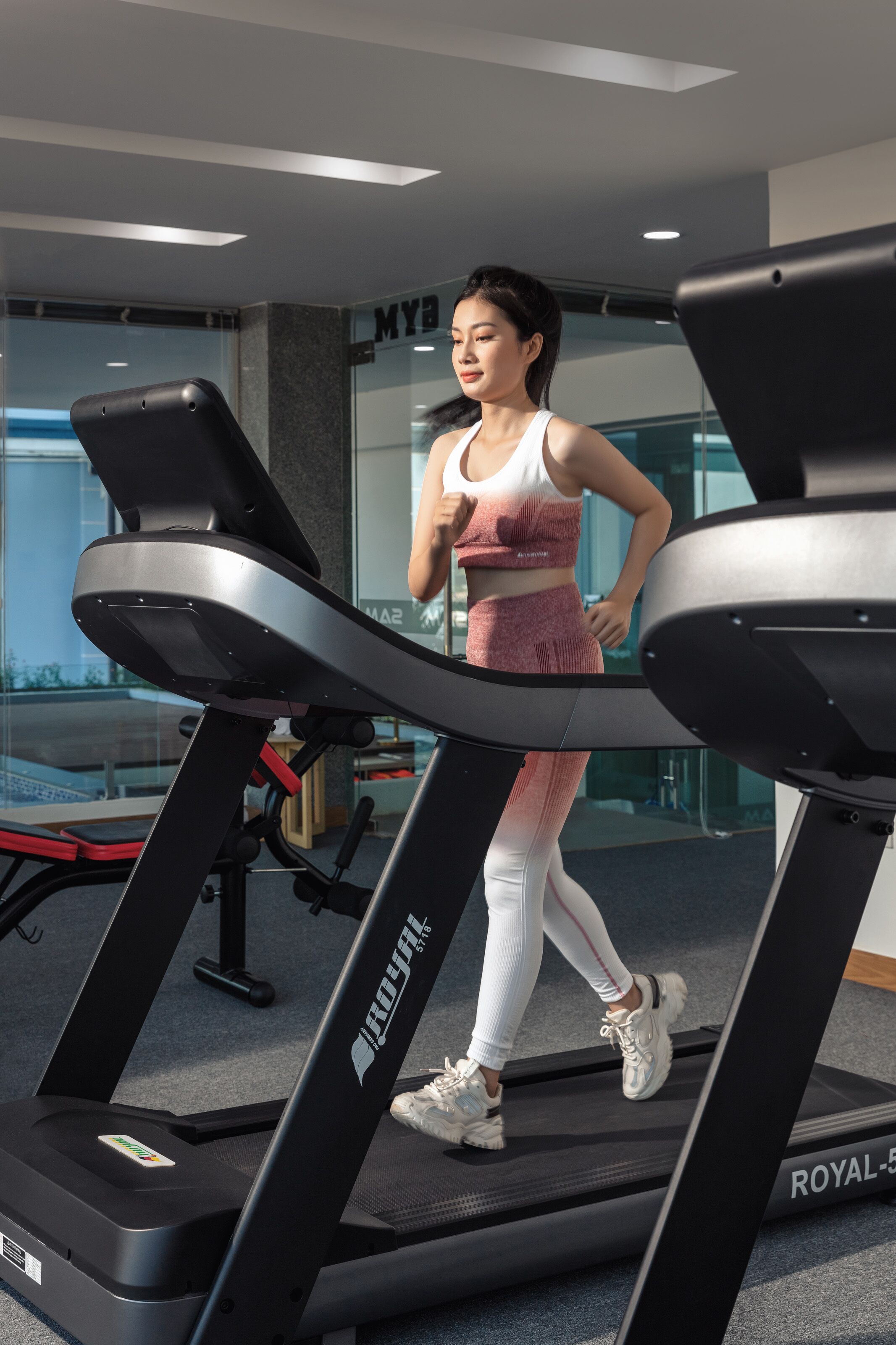 A woman walking on a treadmill in a gym with a visible logo on the machine.