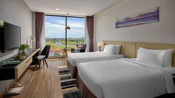A hotel room with two beds, a desk, a TV, and a large window with a view of a body of water and a cityscape.