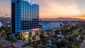 Un moderno edificio hotel con un grande cartello 'SAM', ampie finestre in vetro e un ingresso ben illuminato.