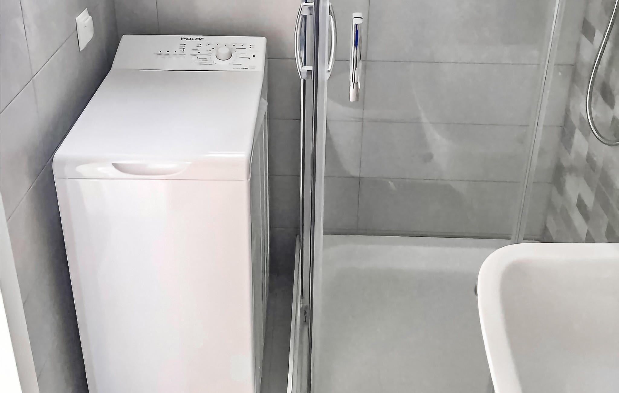 A compact bathroom with a white washing machine, a glass shower enclosure, and a white bathtub.