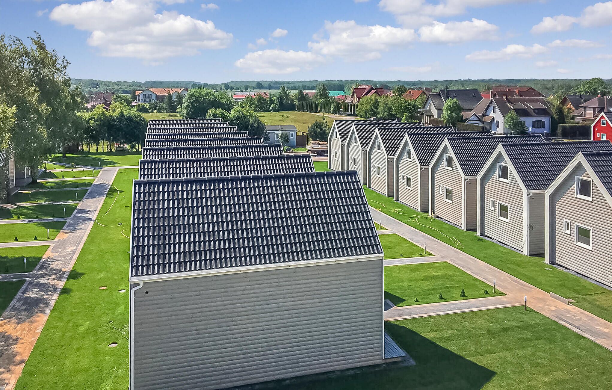 A row of uniform, single-story cabins with a sloped roof, arranged in a neat row with a well-maintained lawn and a clear sky in the background.