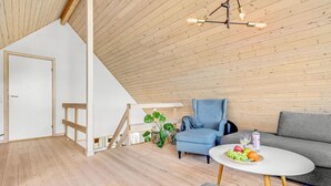 Ein modernes Loft mit freiliegenden Holzbalken, einem blauen Sessel, einem grauen Sofa und einem runden Tisch mit Früchten.